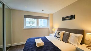Ein Hotelzimmer mit Bett, Fenster, Wandgemälde und Nachttisch mit Lampe.