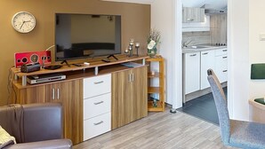 Una sala de estar moderna con una televisión de pantalla plana, un mueble bajo para equipo audiovisual y un comedor con una cocina al fondo.