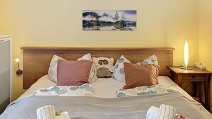 Una cama bien hecha con almohadas estampadas, una lámpara de noche y un cuadro en la pared.