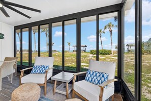 A room with large windows, wicker chairs, a small table, and a view of the beach.