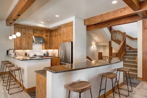 Eine Küche mit Holzschränken, einem Edelstahlkühlschrank, einer Granit Arbeitsplatte und Barhocker.