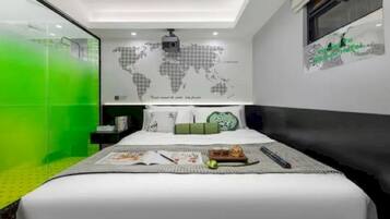 A modern hotel room with a bed, a world map on the wall, and a green glass partition.