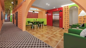 A hotel lobby with a patterned floor, a green dining area, a red wall with a number board, and a green sofa. - Boni Hotel Guangzhou Huangsha Station (Guangzhou)