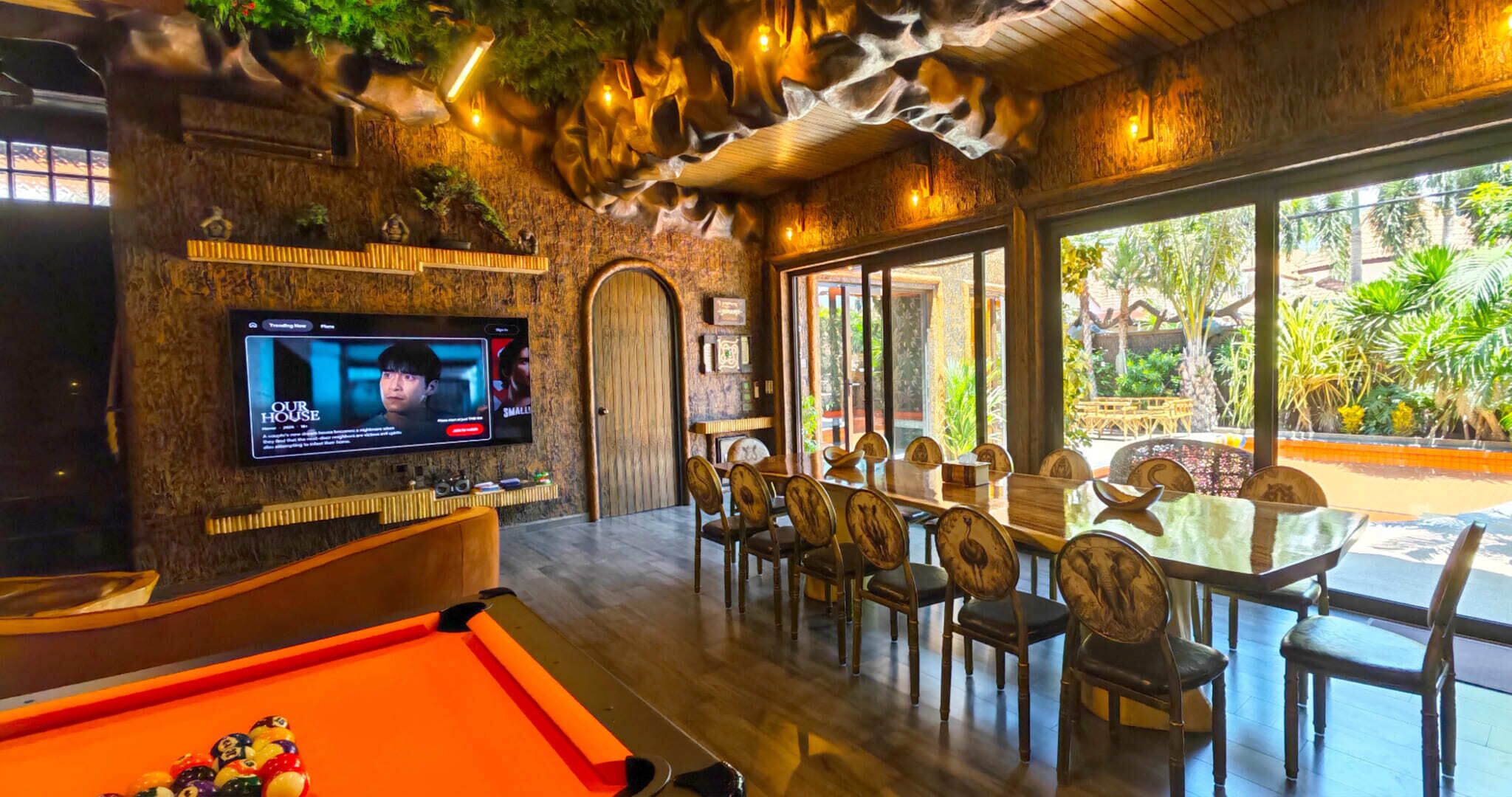 A pool table, a television screen, and a dining area with chairs and a table.