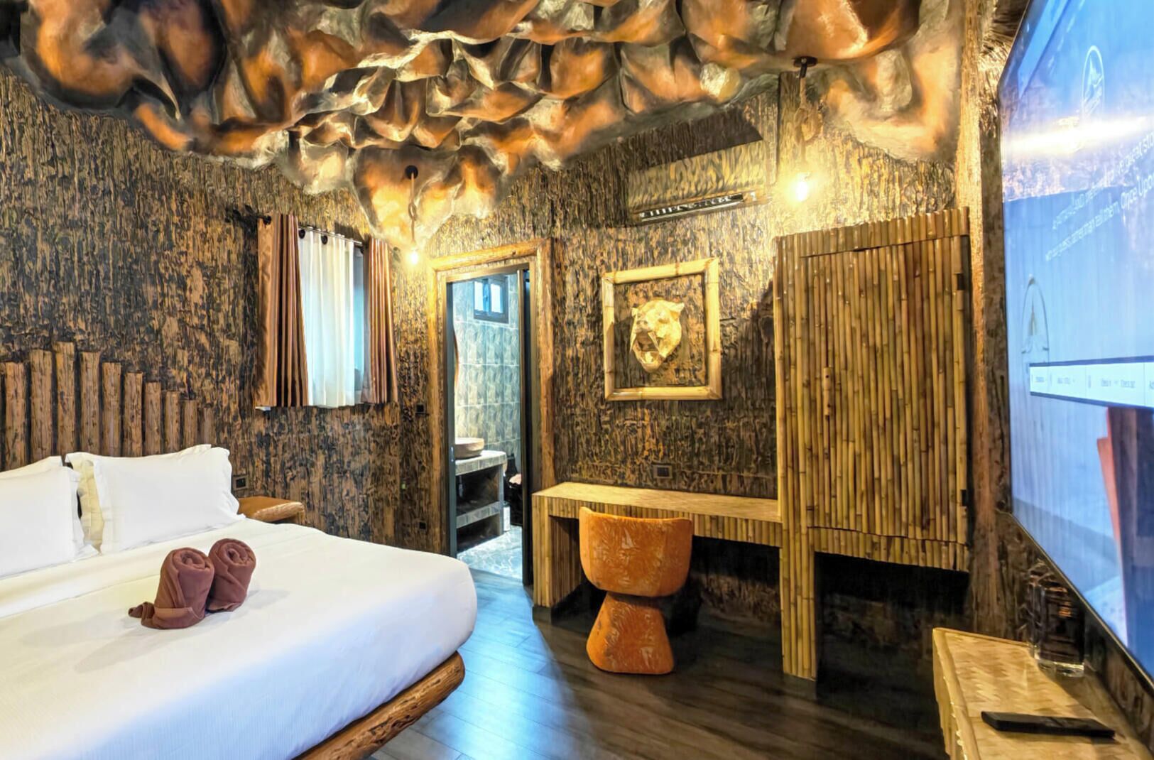 A room with a large bed, a wooden bench, a stone sink, and a wall with a skull decoration.