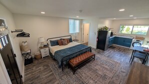 A bedroom with a bed, bedside tables, a bench, a rug, a kitchen with a fridge, stove, and sink, and a window with a view.