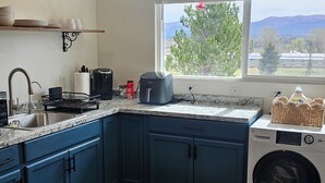 A kitchen with dark blue cabinets, a built-in washing machine, a window with a view of trees and mountains, and a countertop with various appliances and items.