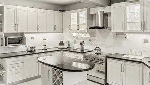 Une cuisine moderne avec des meubles blancs, un îlot central, un four encastré et un four à micro-ondes.