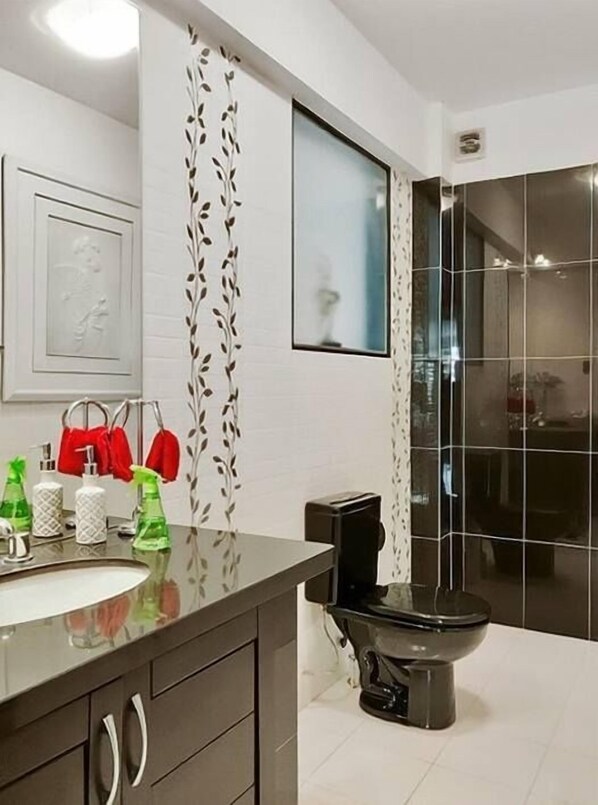 Un baño moderno con un inodoro negro, un lavabo blanco con espejo y una zona de ducha.