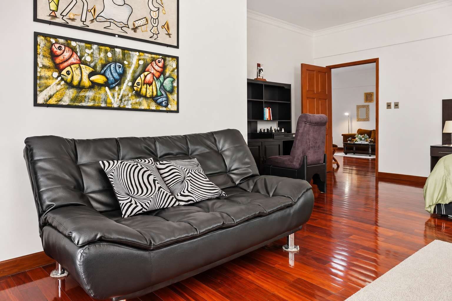 A modern living room with a black leather sofa, zebra-patterned cushions, and two abstract paintings on the wall.