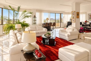 A spacious living room with white sofas, a red rug, and a large window offering a city view. - Recoleta 3BR Penthouse | Rooftop, Sauna, Jacuzzi (Cochabamba)