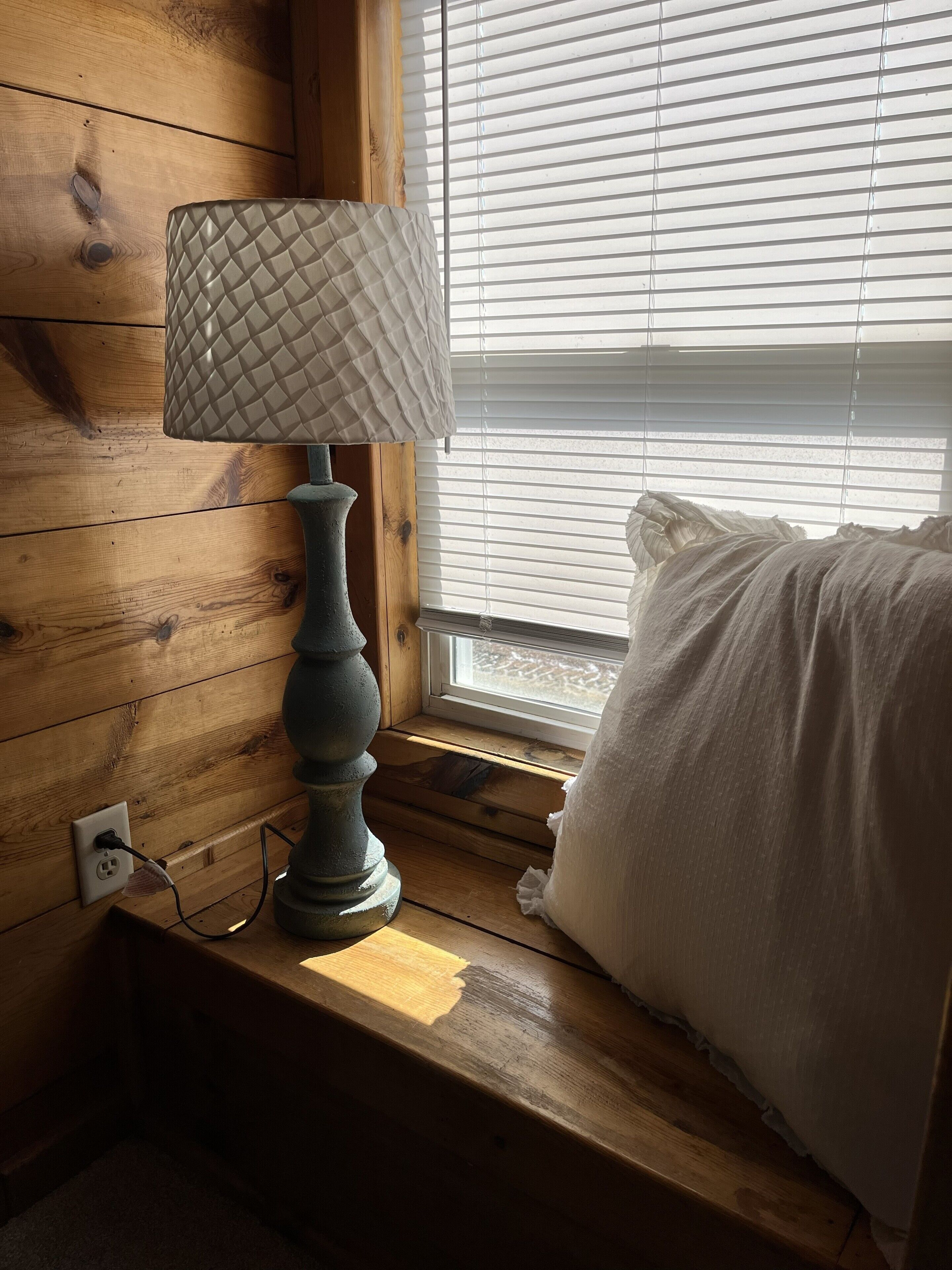 Una cama de madera con ventana, una lámpara y un enchufe.