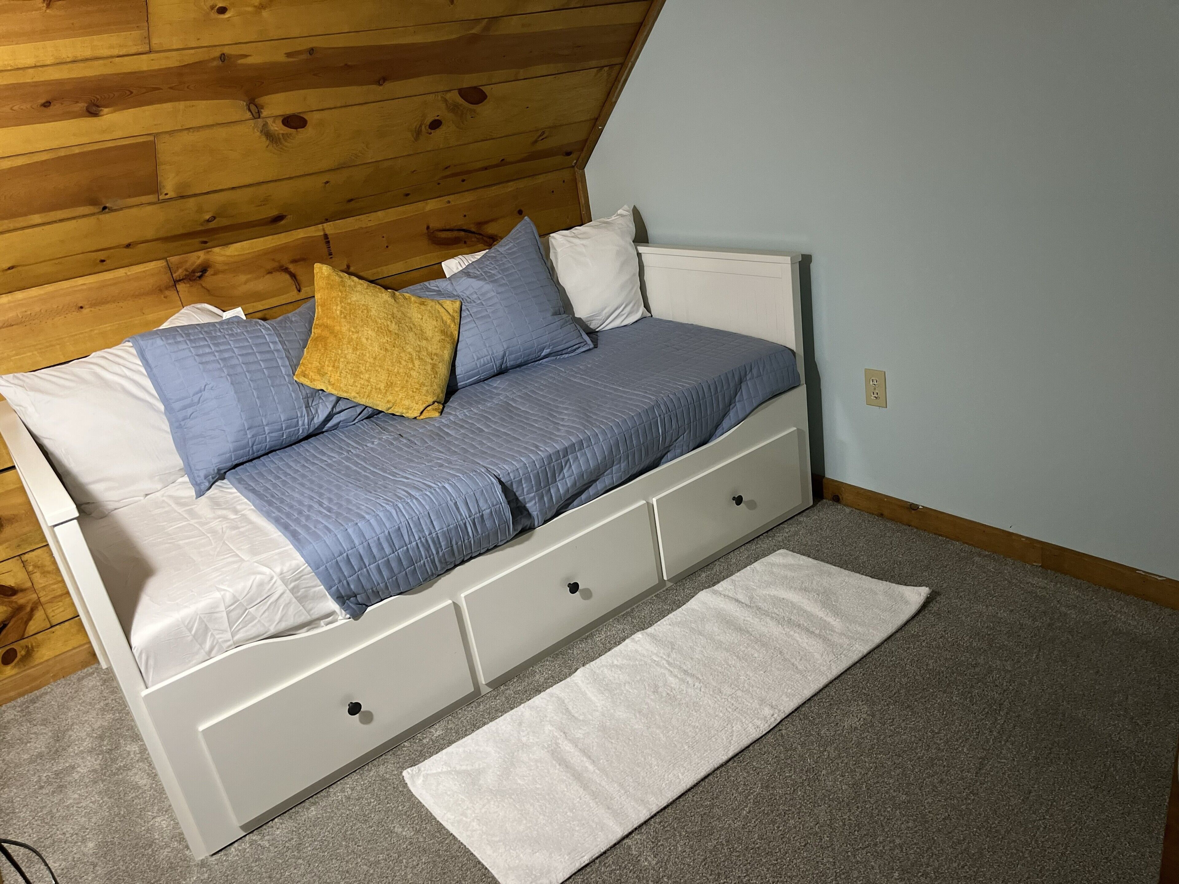 Una cama con cabecera, almohadas y una colcha en una habitación con techo de madera y paredes azul claro.
