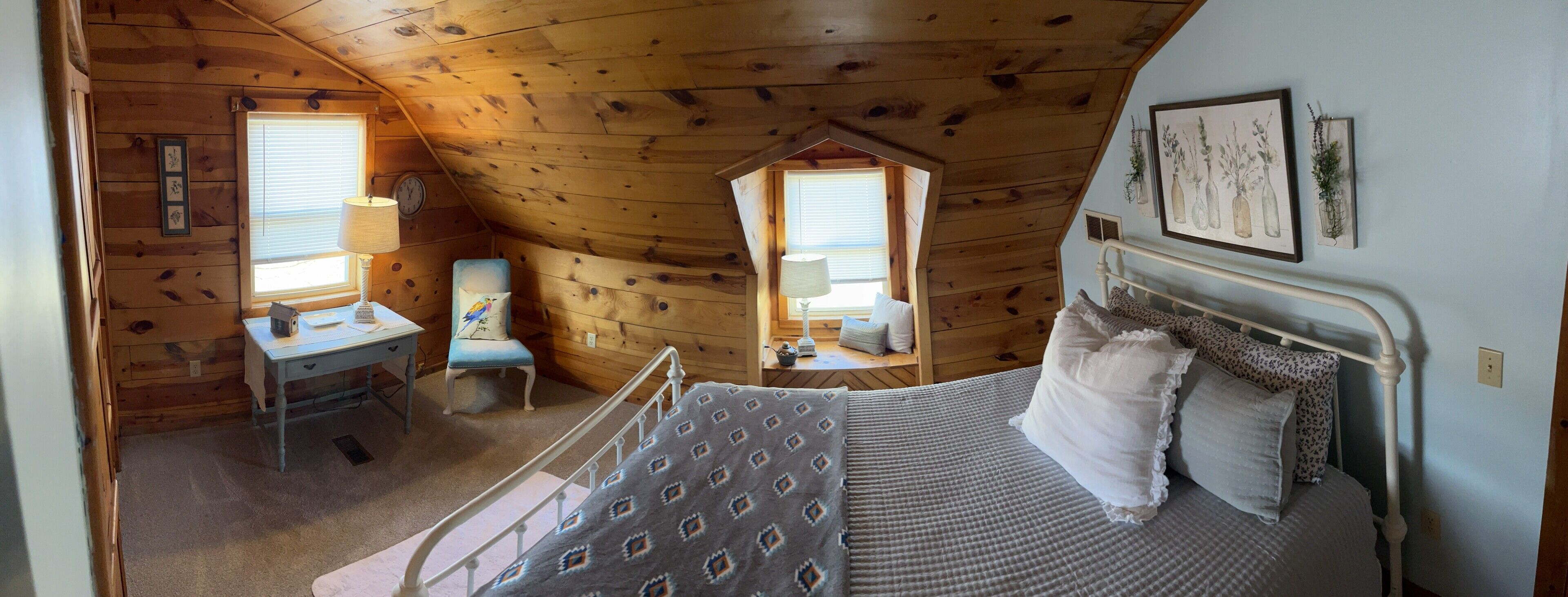 Ein Schlafzimmer mit einem Bett, einem Schreibtisch, einem Stuhl und zwei Fenstern.
