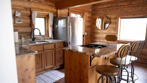 Interior de una cabaña de madera con cocina, que incluye un refrigerador, pileta y taburetes de bar.