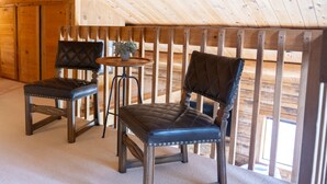 Interior de una cabaña de madera con dos sillones de cuero, una mesita con una planta y vistas al exterior.