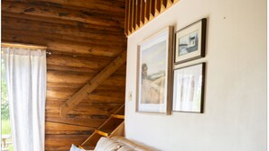 Una habitación con techo de madera, un sofá beige con almohadones, una ventana con cortinas y dos cuadros en la pared.