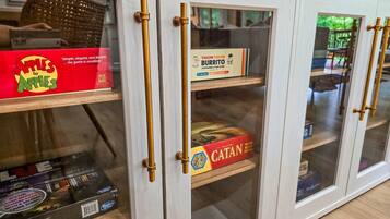 Ein Schrank mit Glastüren und Messinggriffen, der Gesellschaftsspiele wie Apples to Apes, Throw Throw Burrito und Catan beherbergt.