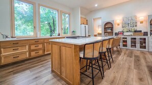 A modern kitchen with wooden cabinets, a central island, bar stools, and large windows.