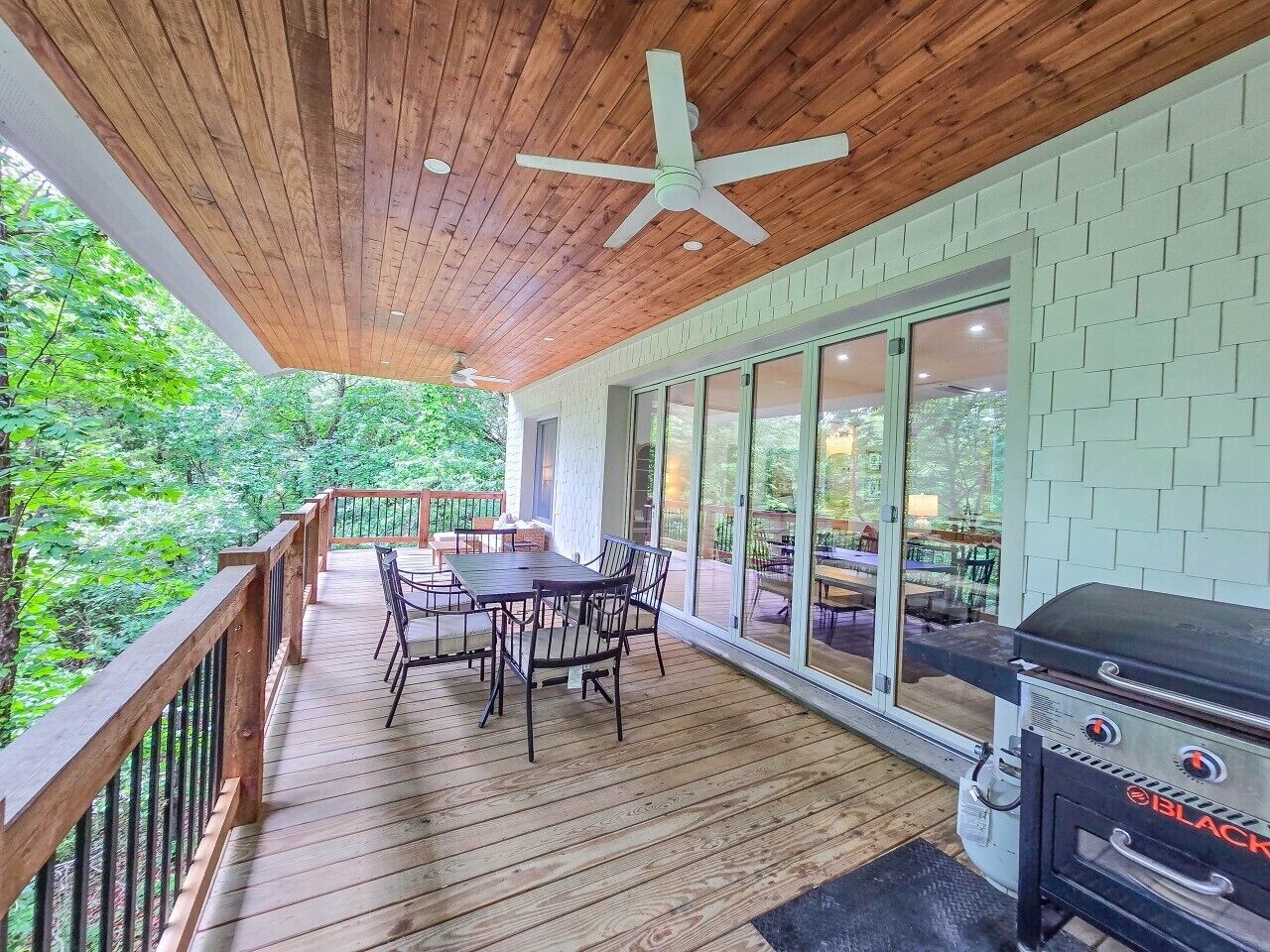 A covered outdoor deck with a table and chairs, a grill, and a star ceiling fan.