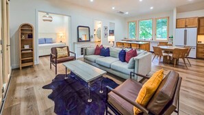 A modern living room with a sofa, coffee table, and chairs. There is a kitchen area with a dining table and chairs.