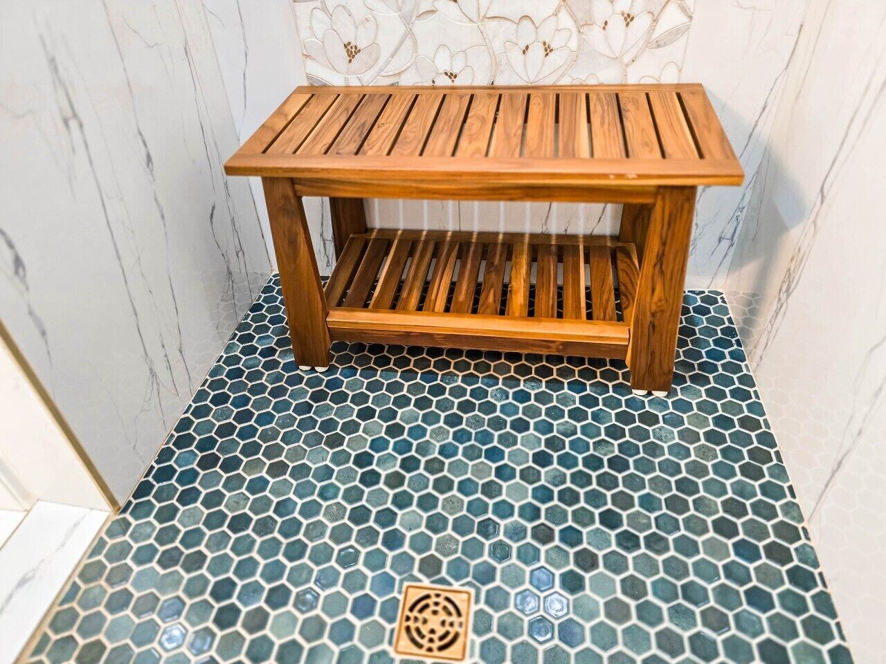 A wooden bench with a slatted design, placed on a tiled floor with a hexagonal pattern.