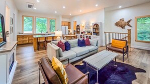 A spacious living area with a sofa, coffee table, and a dining table. There is a kitchen area with cabinets and a refrigerator.