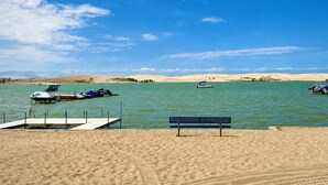 Una playa arenosa con un banco y un muelle con barcos.