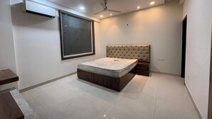 A bedroom with a bed, a ceiling fan, recessed lighting, and a large window. - Hotel Twamev Peeragarhi (New Delhi)