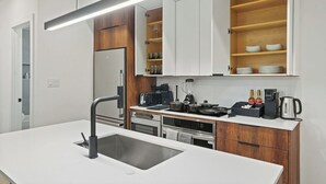 Une cuisine moderne avec des meubles blancs, un four encastré, un évier et un plan de travail équipé de divers appareils et ustensiles.