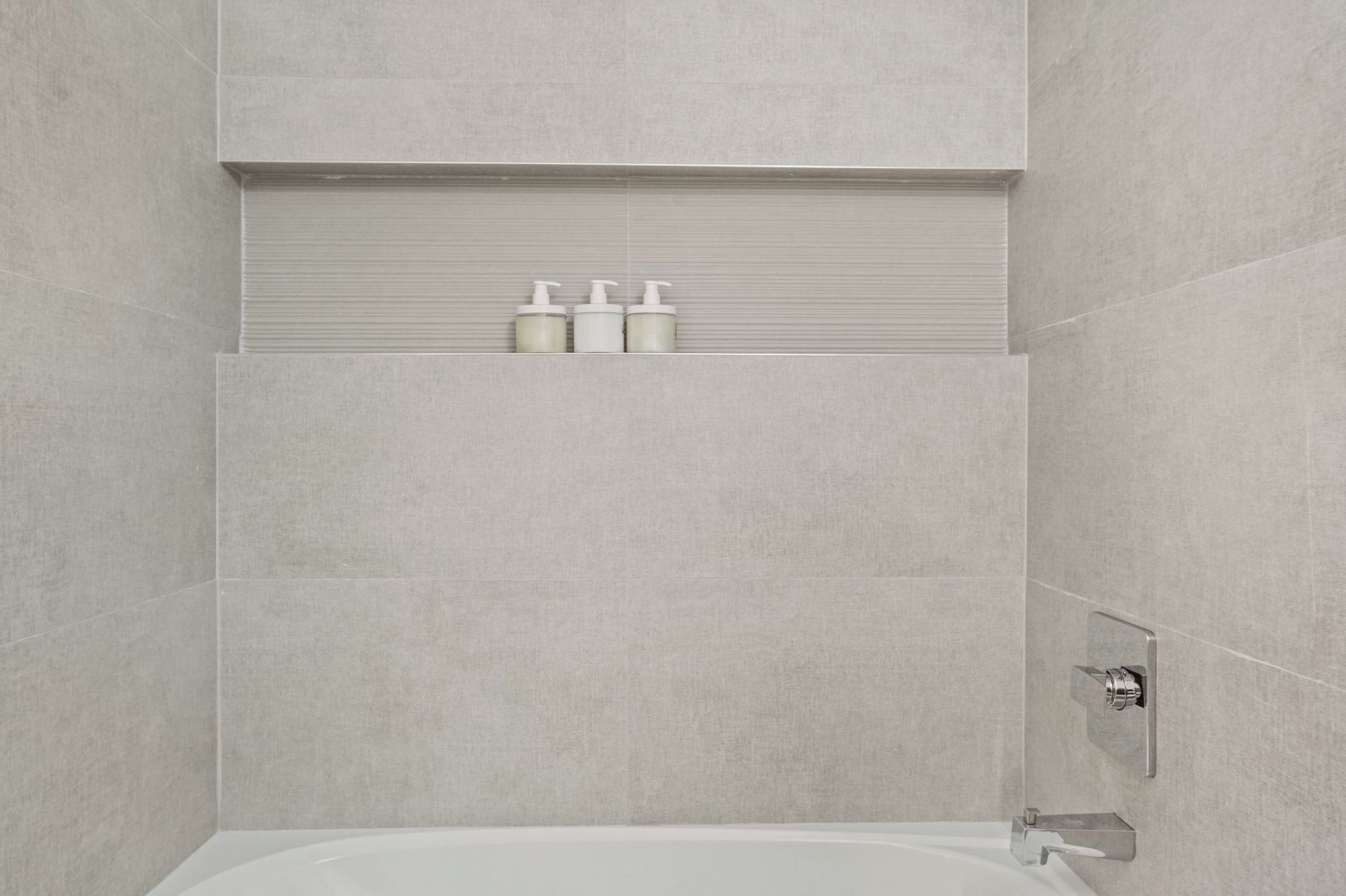 A modern bathroom with a bathtub, a towel rack, and a shelf with toiletries.