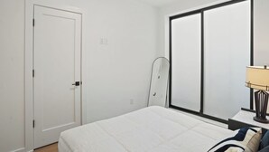 Une chambre à coucher avec un lit, une fenêtre, une porte et une table de chevet avec une lampe.