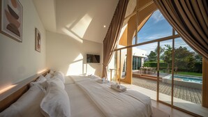 A large bed with white linens, a TV on the wall, and a view of a swimming pool. - Winvilla Pattaya - Private Pool Villa 5 Bedrooms (Bang Lamung)