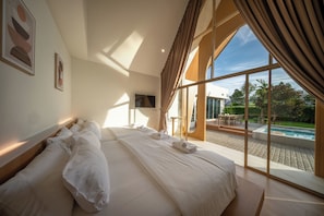 Una cama grande con ropa blanca, un televisor en la pared y vistas a una piscina.
