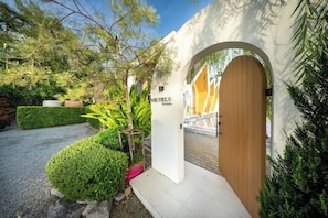 A building entrance with an arched doorway, a sign with Chinese characters, and a well-maintained garden with various plants. - Winvilla Pattaya (Bang Lamung)