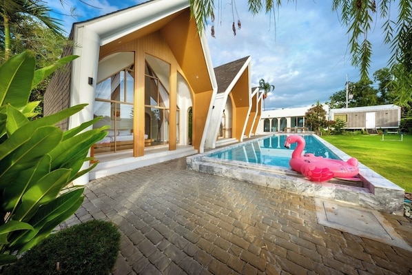 Una casa moderna con piscina, un flotador de flamenco rosa y un césped bien cuidado.
