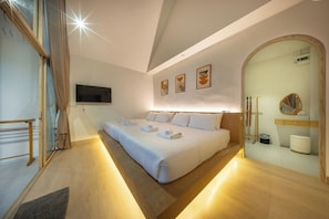 Ein Schlafzimmer mit einem großen Bett, einem an der Wand montierten Fernseher und einem durch einen Bogen sichtbaren Badezimmer.