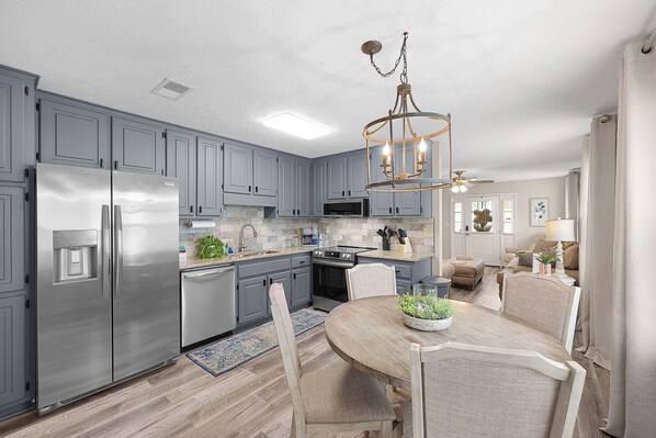 A modern kitchen with grey cabinets, stainless steel appliances, and a wooden dining table.