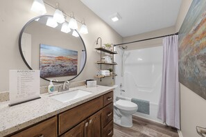 A bathroom with a large mirror, a sink, a toilet, a shower, and a painting on the wall.