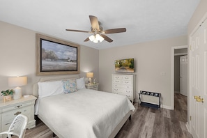 A bedroom with a bed, nightstands, a dresser, a ceiling fan, and a door leading to another room.
