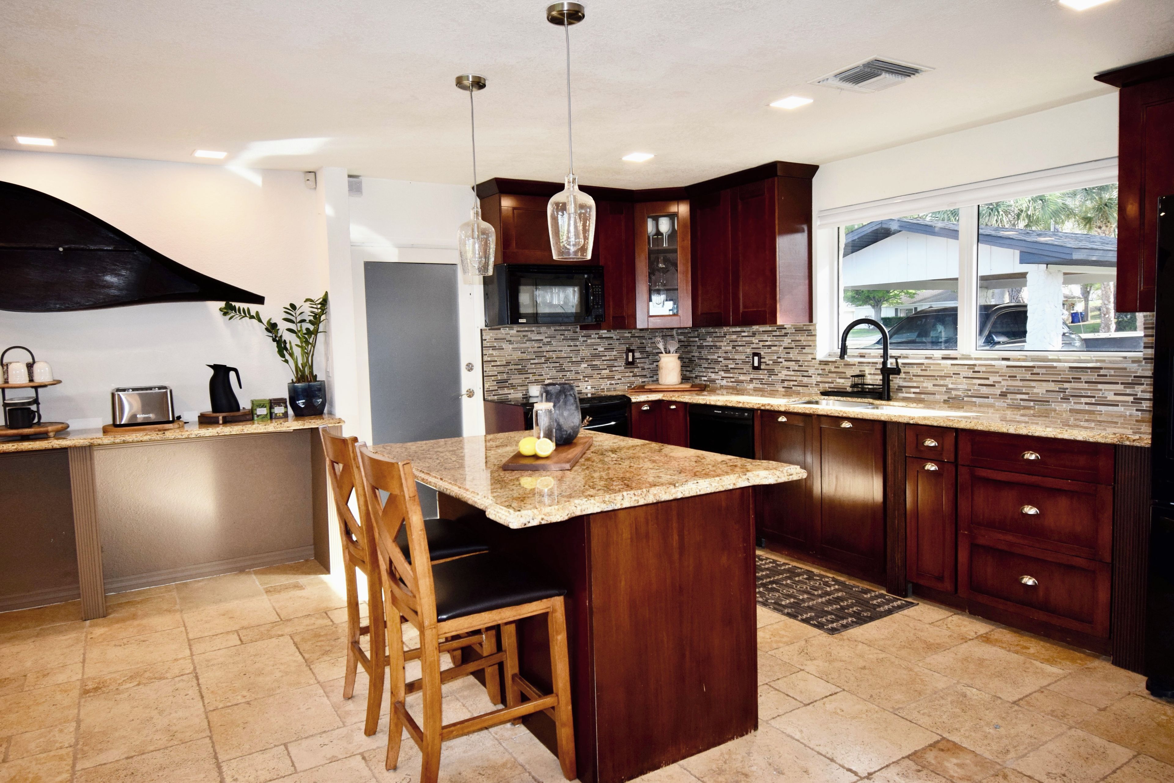 A modern kitchen with a central island, dark wood cabinets, a granite countertop, and pendant lighting.