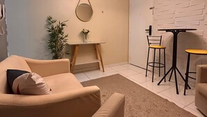 Uma sala de estar moderna com sofá, uma mesinha com cadeiras, luminária pendente e espelho fixado na parede.