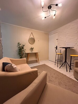 Ein modernes Wohnzimmer mit einer Couch, einem kleinen Tisch mit Stühlen, einer Hängeleuchte und einem an der Wand befestigten Spiegel.