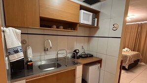 Uma cozinha compacta com armários de madeira, micro-ondas, pia e uma pequena geladeira.