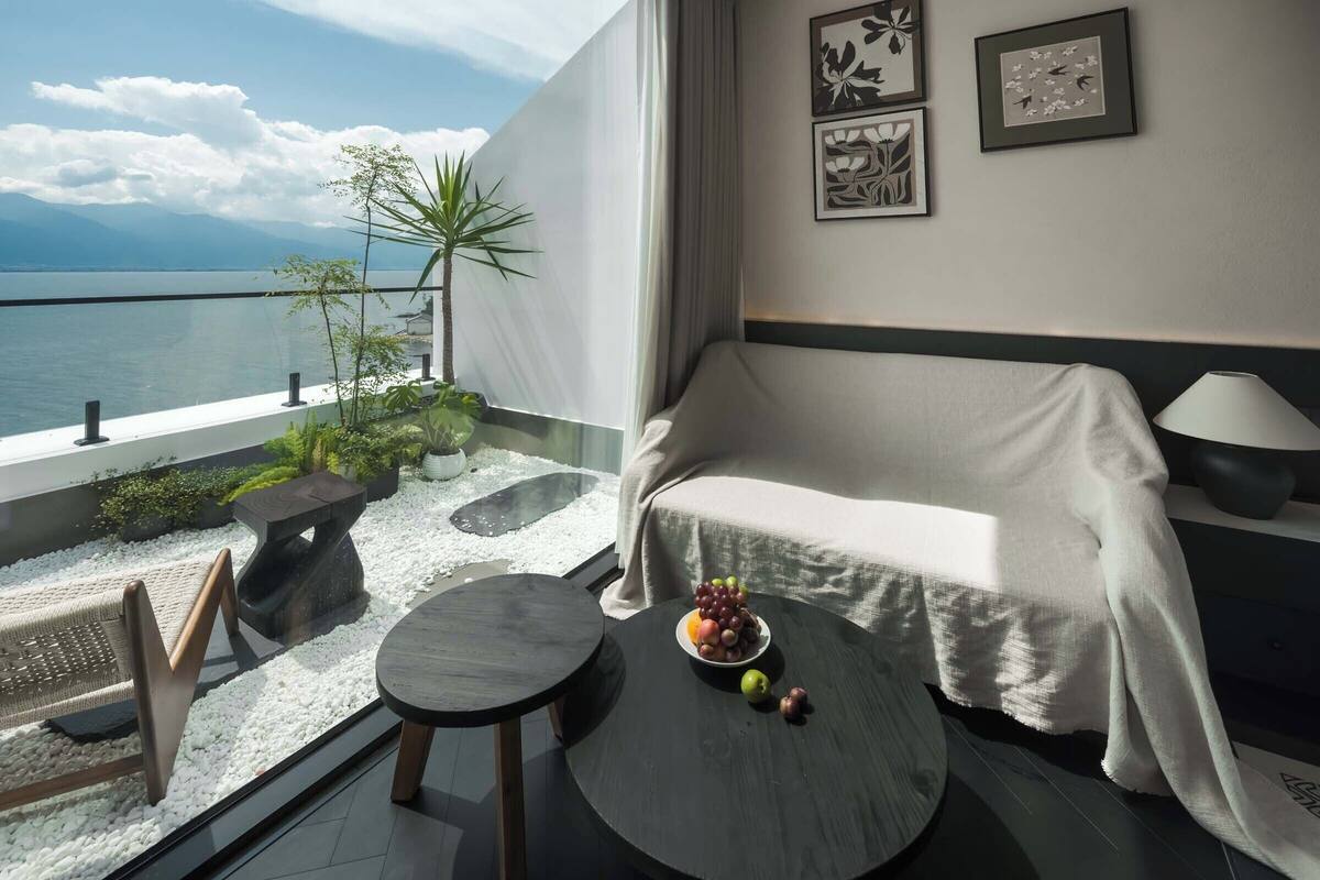 A balcony with a view of the sea, a sofa, a small round table with fruit, and two framed artworks on the wall.