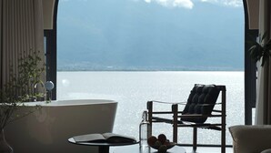 A room with a bathtub, a chair, a table with fruits, and a view of a body of water. - Dali Azure Hillside Boutique Resort- Wenbi Village - Gourmet Dining & Cocktail Lounge & Complimentary Airport Pick-up for 2 Nights (Dali)