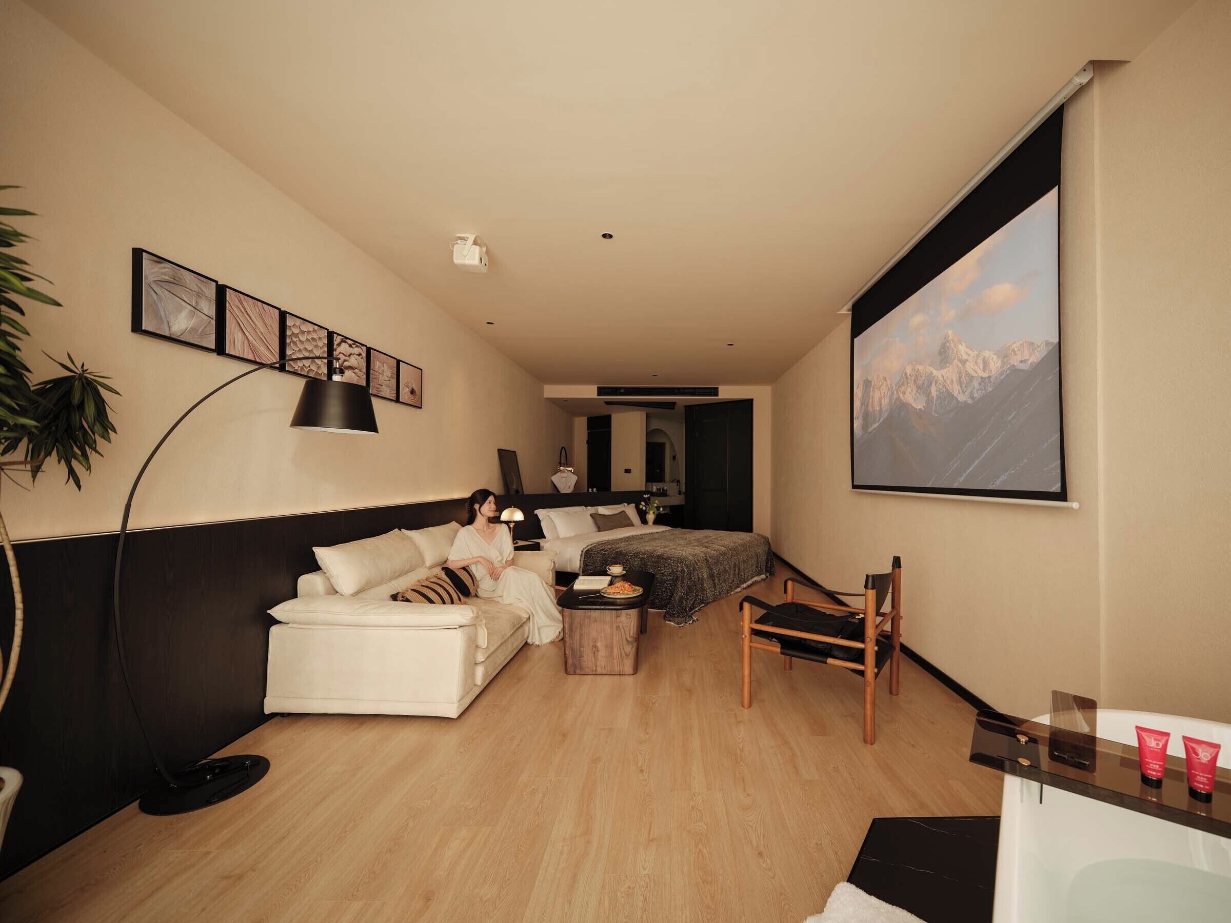 Una habitación de hotel moderna con sofá, mesa de comedor, silla, cama, televisor y un gran ventanal con vista a la montaña.
