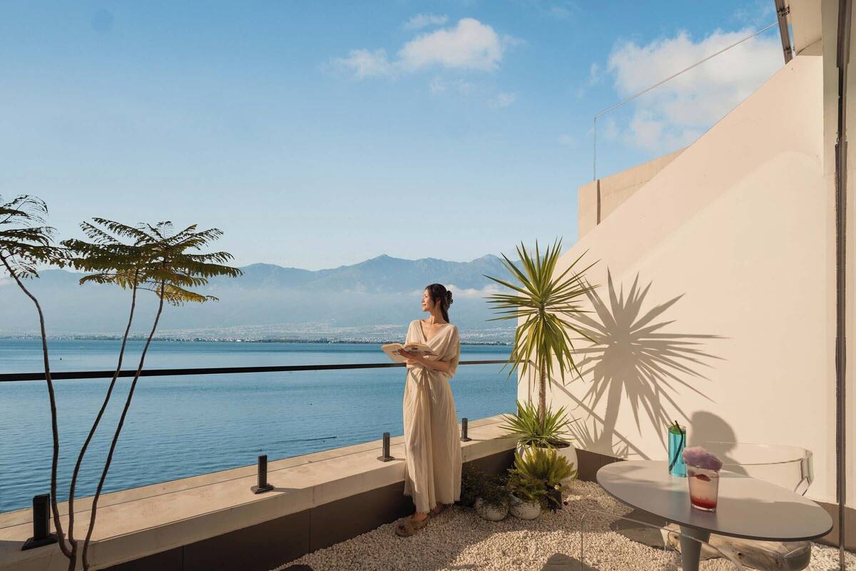 A balcony with a view of the sea, a table with a drink, and potted plants.