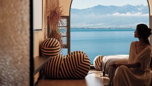 A room with a large arched window, a potted plant, striped bean bags, and a view of a body of water and mountains. - Dali Azure Hillside Boutique Resort- Wenbi Village - Gourmet Dining & Cocktail Lounge & Complimentary Airport Pick-up for 2 Nights (Dali)