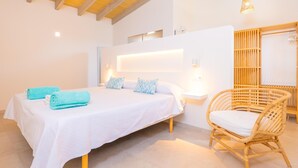 Ein Schlafzimmer mit einem Bett, einem Sessel, einem Nachttisch, einem Wandregal und einer Pendelleuchte.